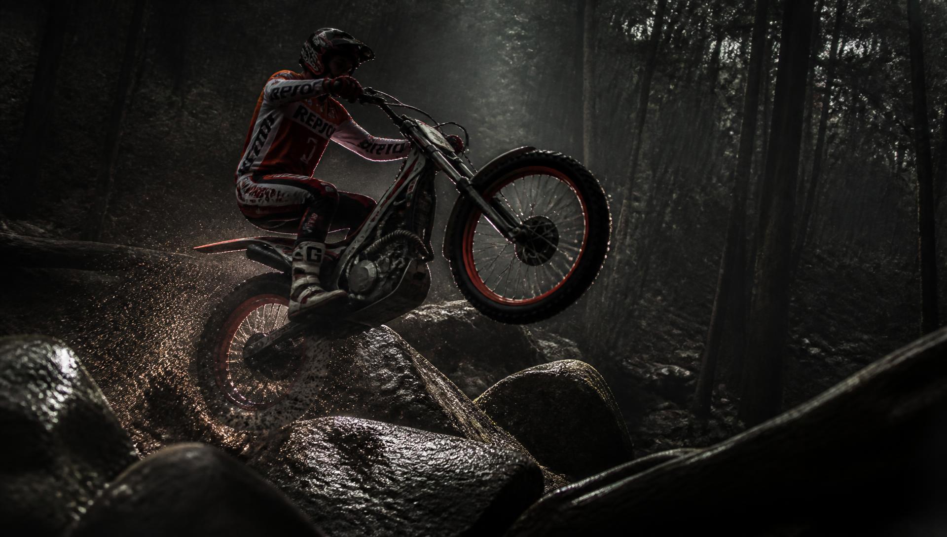 Trials motorcycle rider tackling wet rocks in woodland